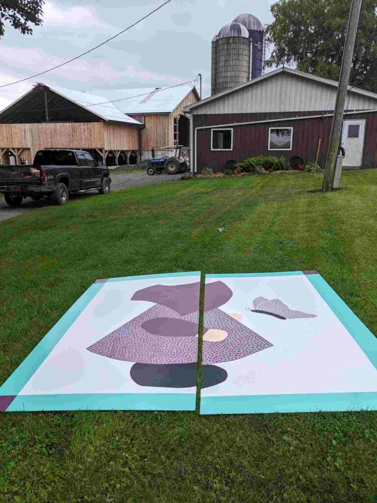 Sunbonnet Sue barn quilt laying on the ground in front of the barn